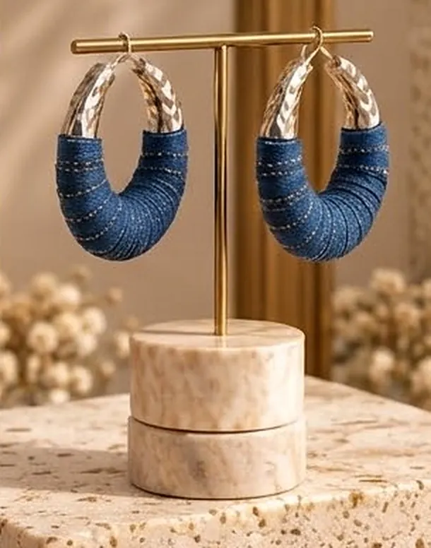 Denim-wrapped rhodium hoop earrings on a gold stand